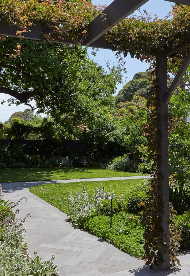 Outdoor lounge area with a pool. Features a white pergola, seating, and lush landscaping.