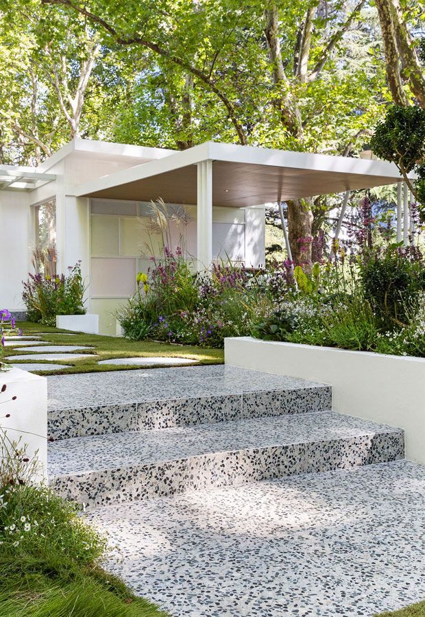 Modern house with pool, shaded patio, and wooden pergola. Turquoise water, glass walls, and dark wood siding.