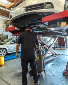 A man is standing under a car in a garage | Driven Auto Care