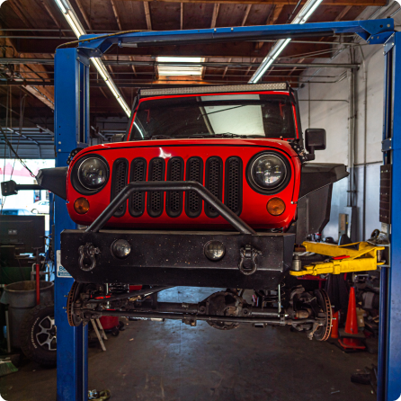 A red jeep is on a lift in a garage | Driven Auto Care