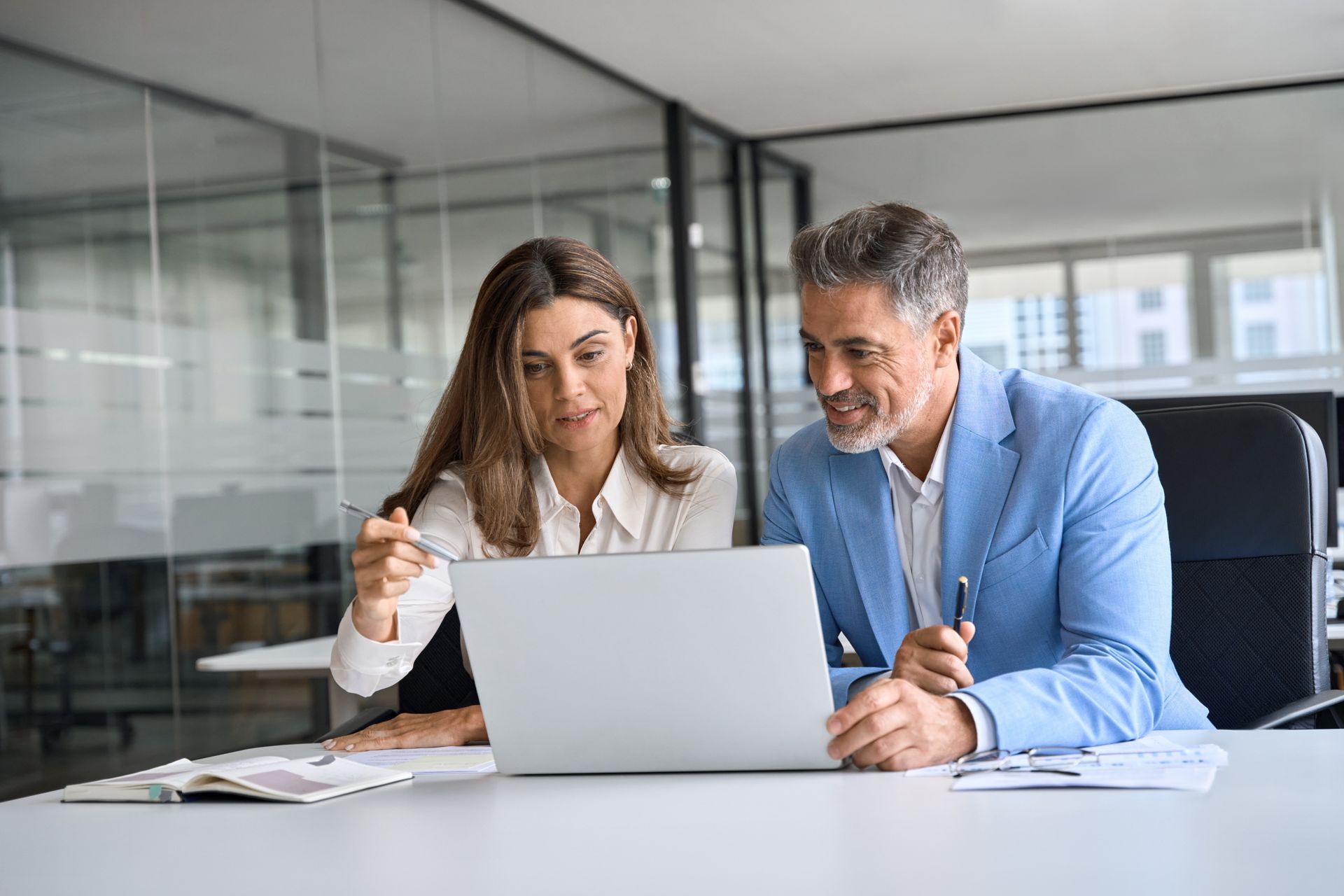 Two colleagues reviewing a laptop in a bright office, discussing work at a desk