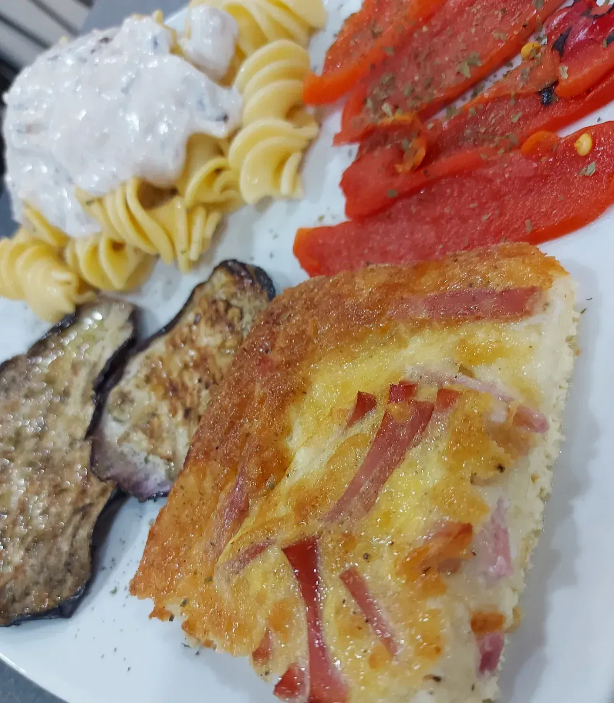 Un piatto bianco sormontato da una fetta di pizza, pasta e verdure