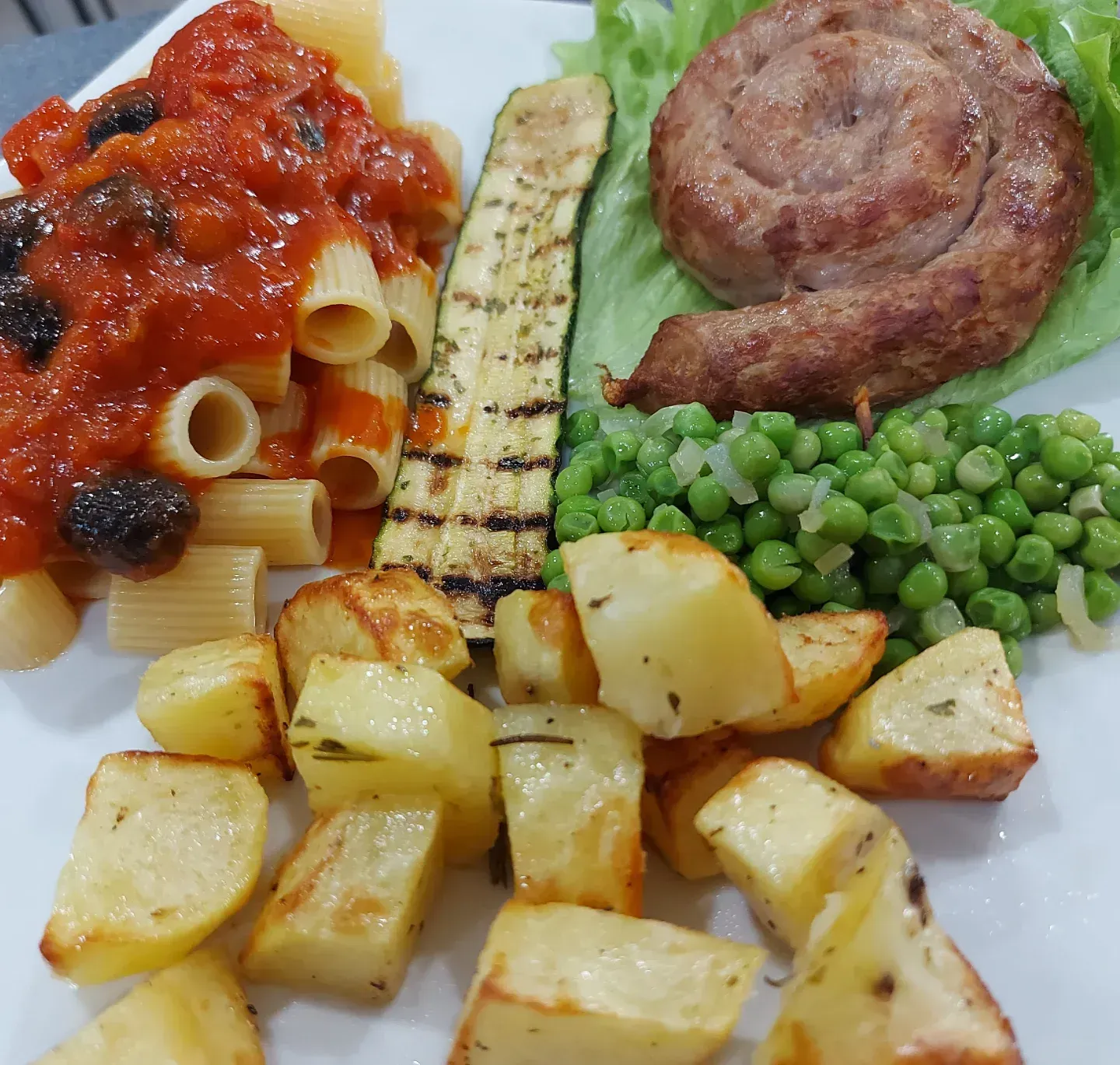 Un piatto bianco con pasta, patate e piselli