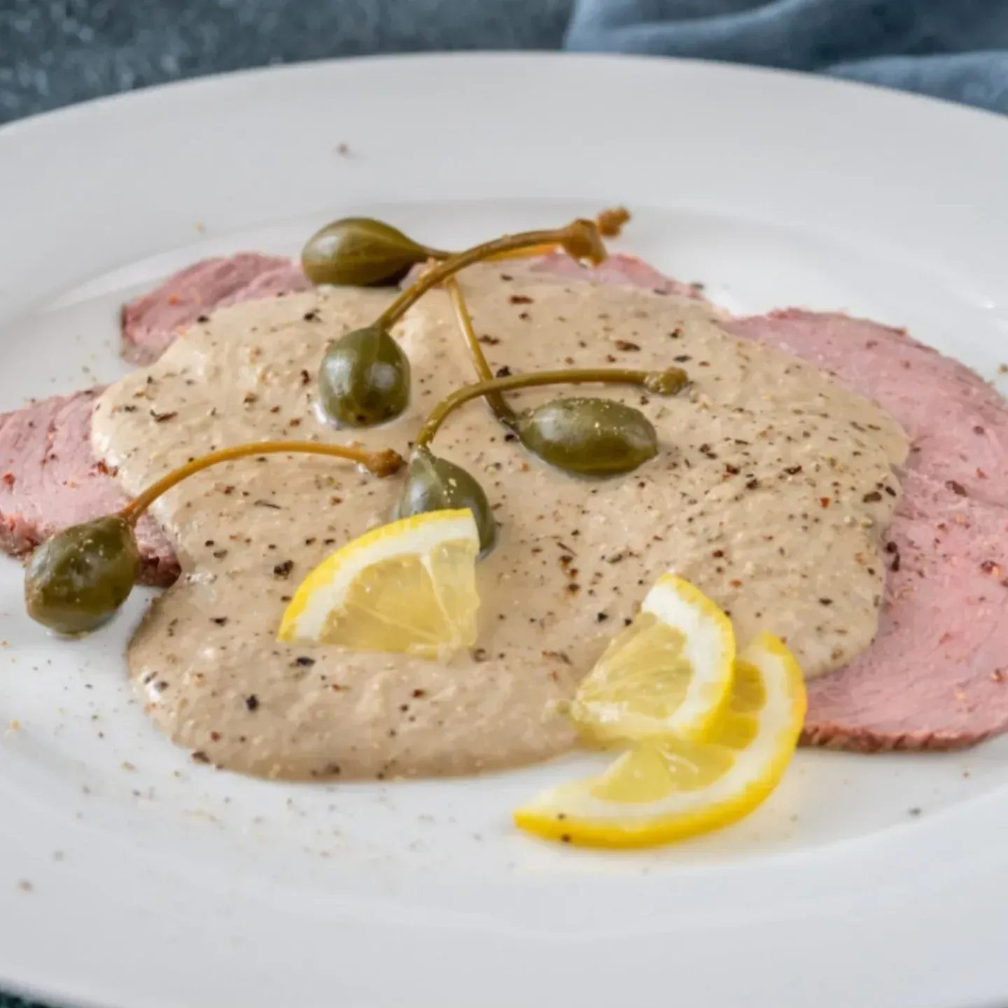 Un piatto bianco condito con ragù di carne, capperi e fette di limone