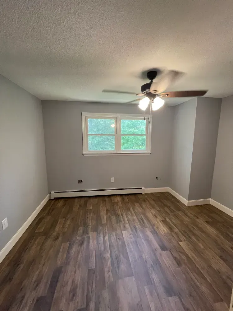 An empty room with hardwood floors and a ceiling fan.