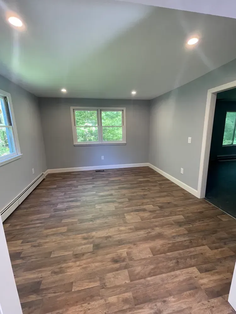 An empty living room with hardwood floors and two windows.