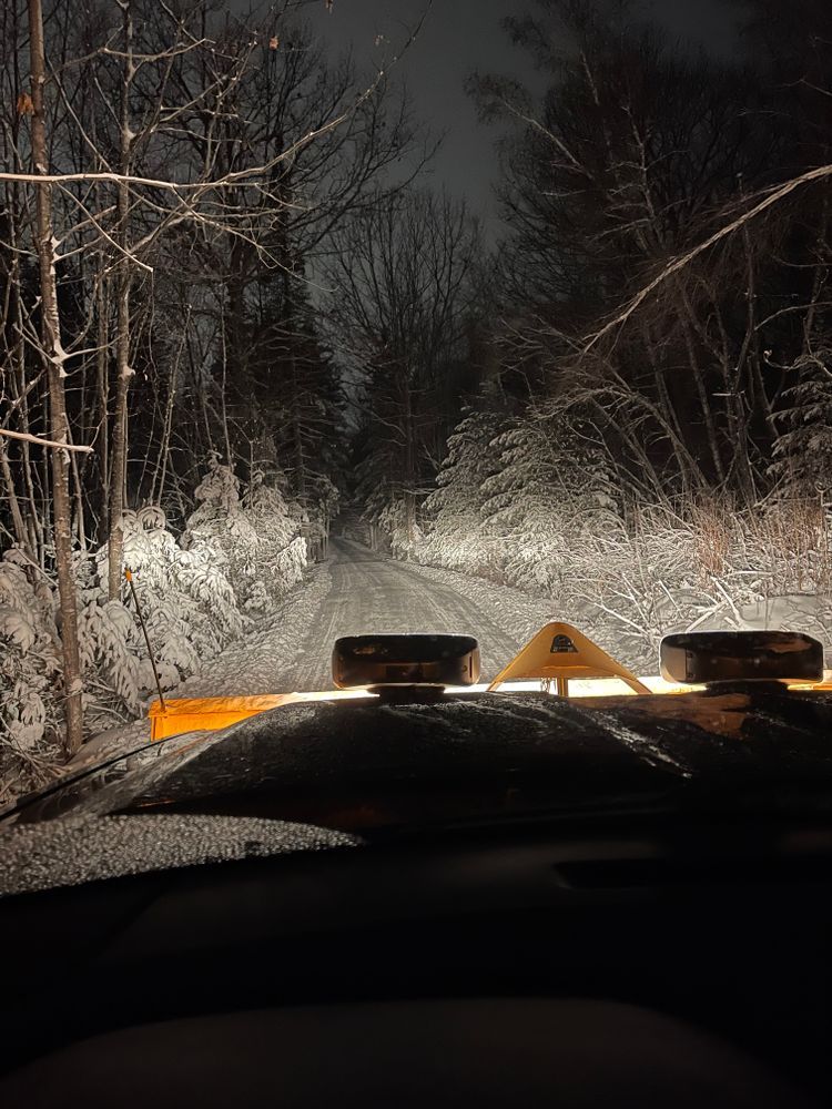 A snow plow is driving down a snowy road at night.