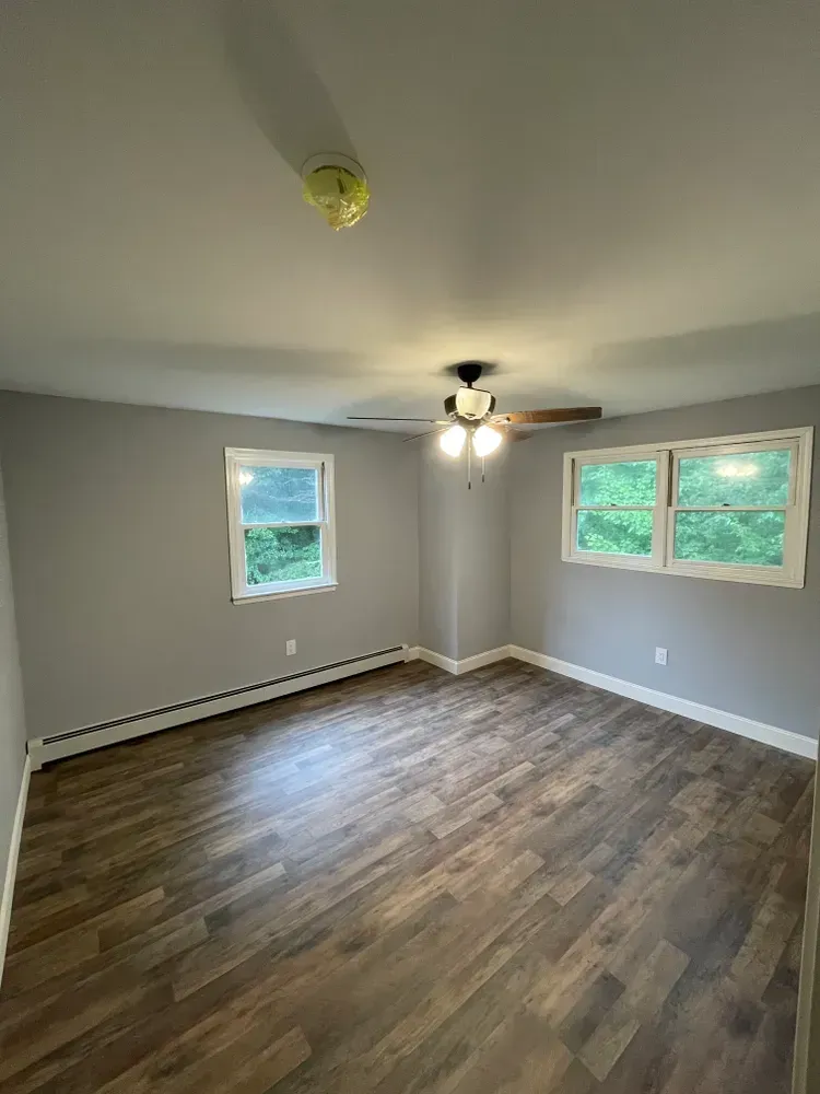 A large empty room with hardwood floors and a ceiling fan.