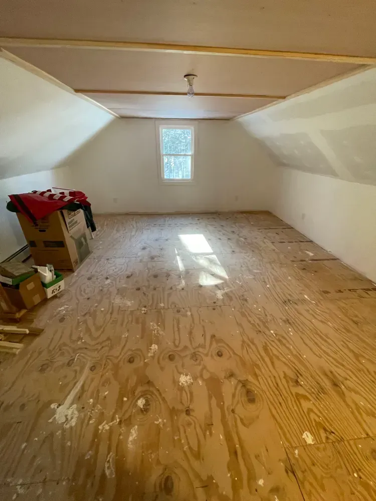 An empty attic with a wooden floor and a window.