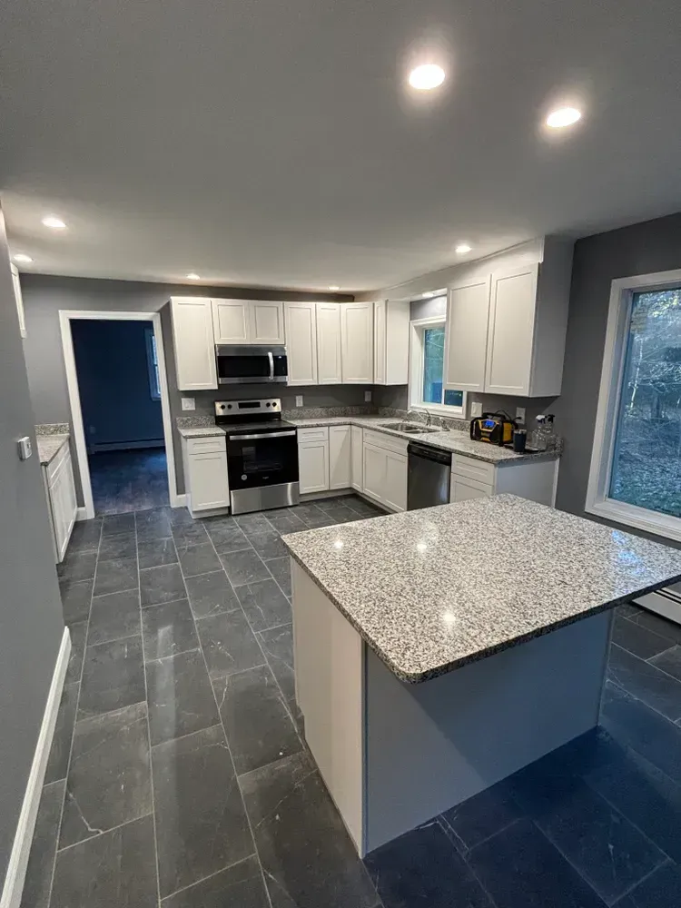 A kitchen with white cabinets , granite counter tops , stainless steel appliances and a large island.