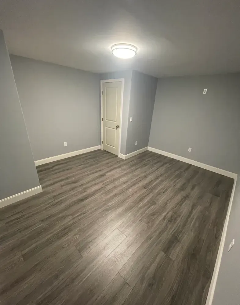 An empty room with hardwood floors and gray walls.