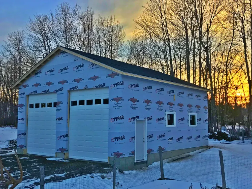 A garage is being built in the snow with a sunset in the background