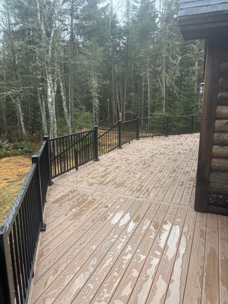 A wooden deck with a black railing and trees in the background.