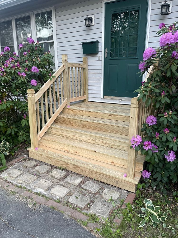 A wooden porch with purple flowers in front of a house.