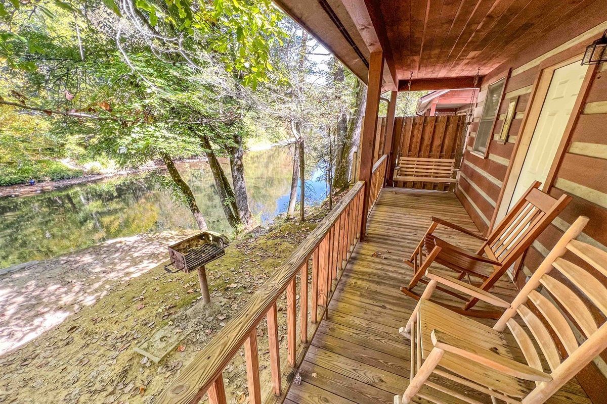 Campsite with picnic table, fire pit, and creek. Trees and greenery surround the area.