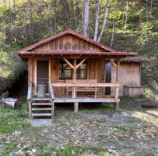 Rustic wooden cabin with porch in a wooded area.