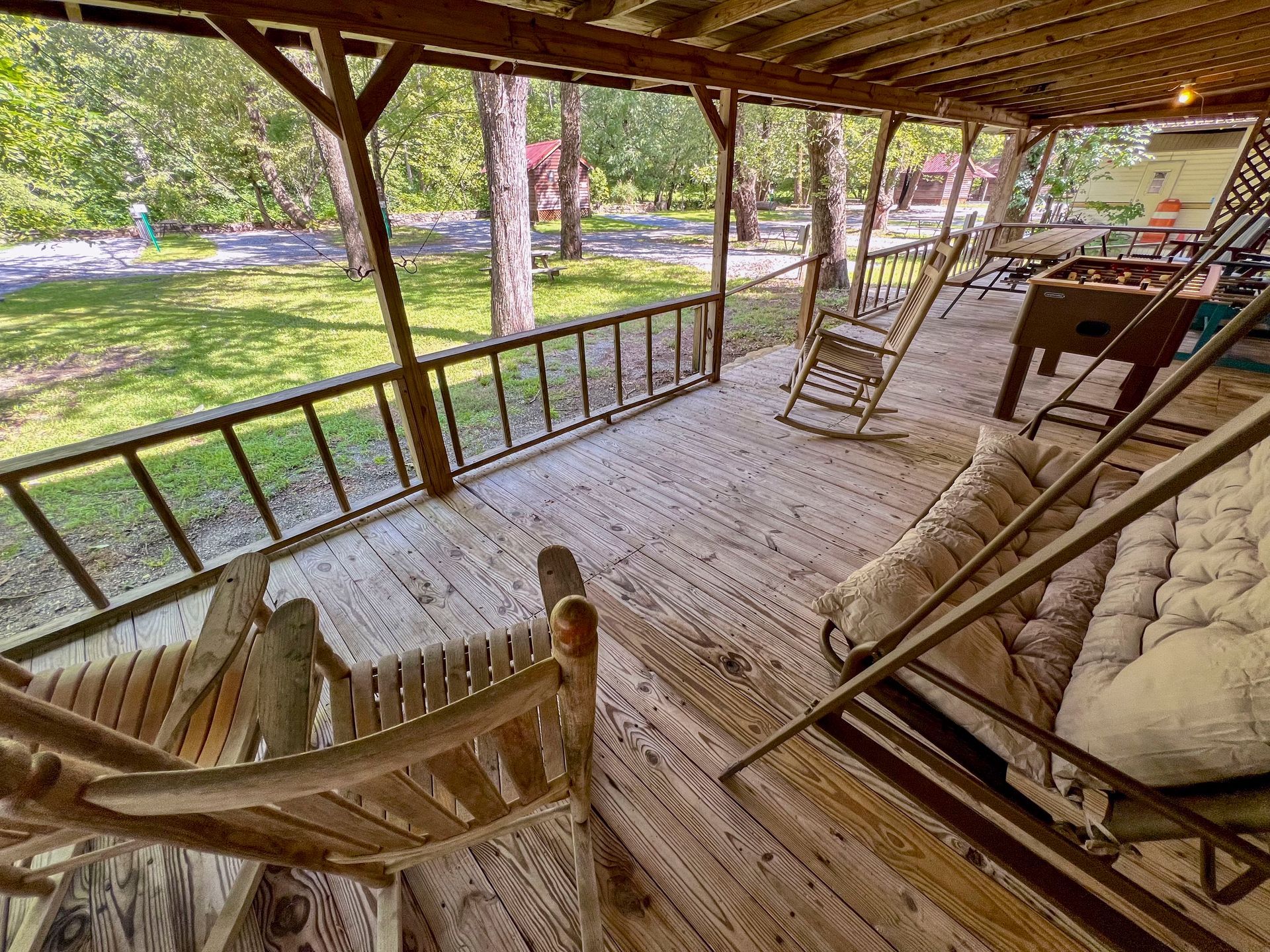Wooden porch with rocking chairs, railing, and stairs, overlooking a grassy area and trees.
