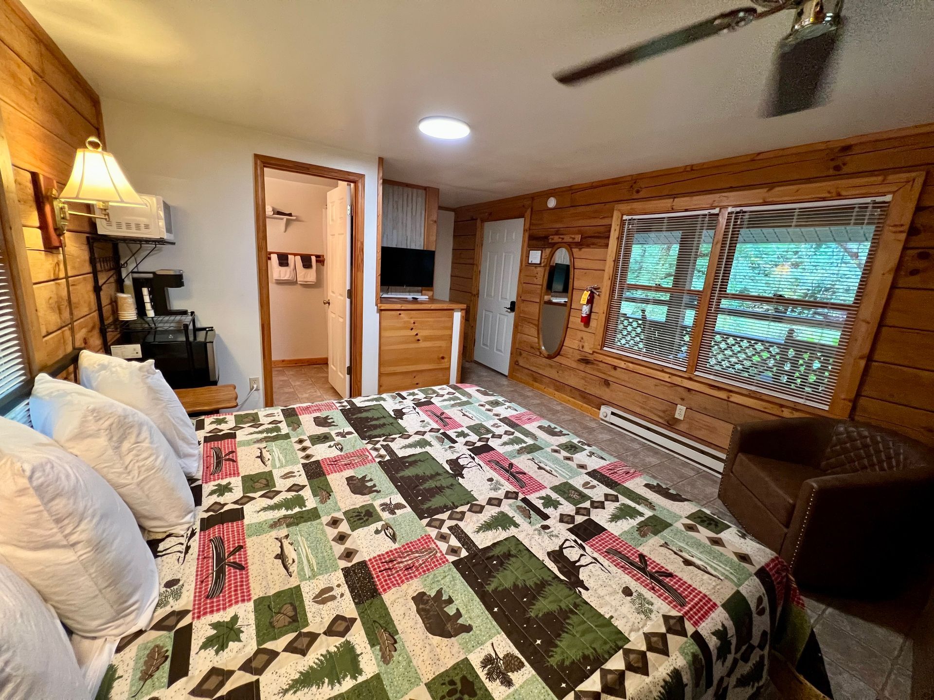 Cozy cabin bedroom with a large bed, wooden walls, and a window overlooking greenery.