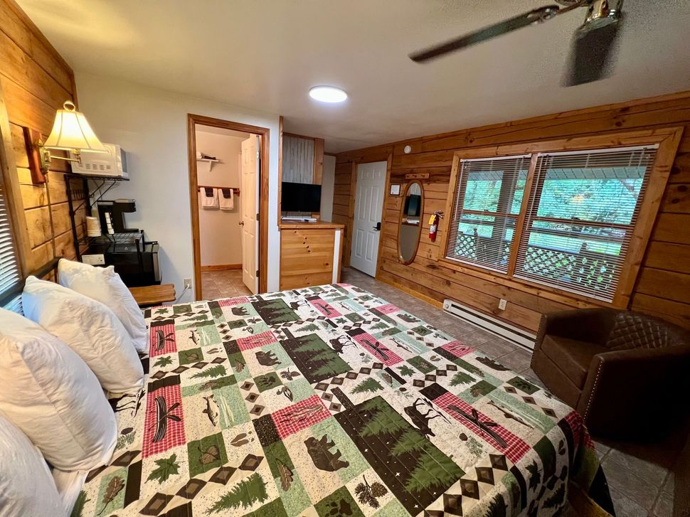 Cozy cabin bedroom with a large bed, wooden walls, and a window overlooking greenery.