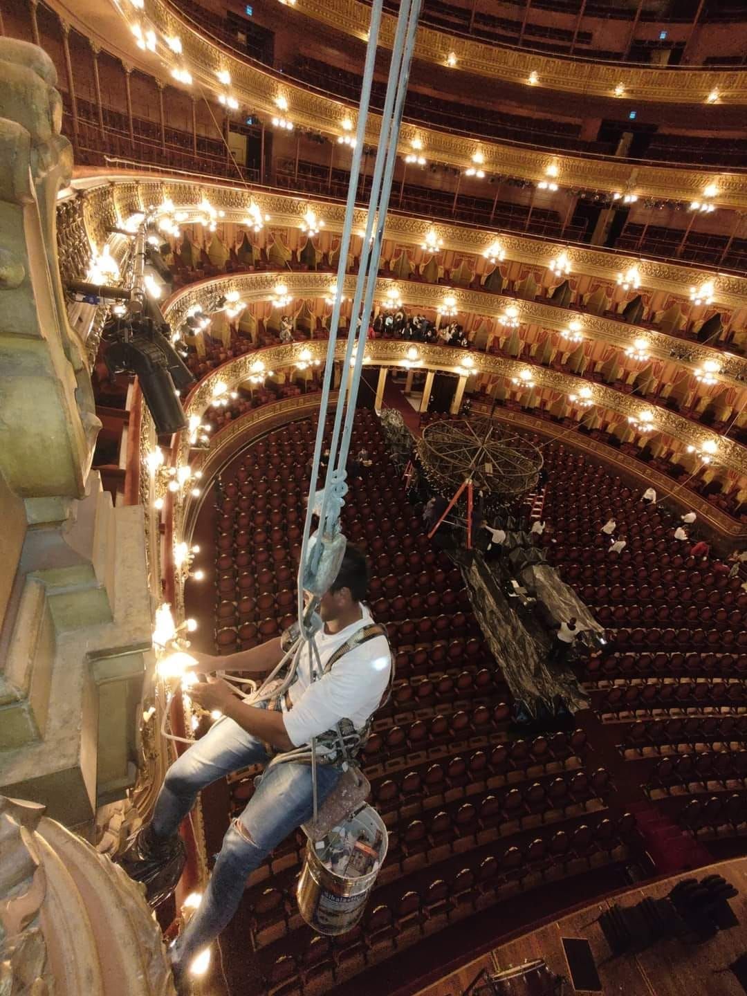 Dos personas con arneses colgando dentro de un teatro, trabajando en la iluminación.