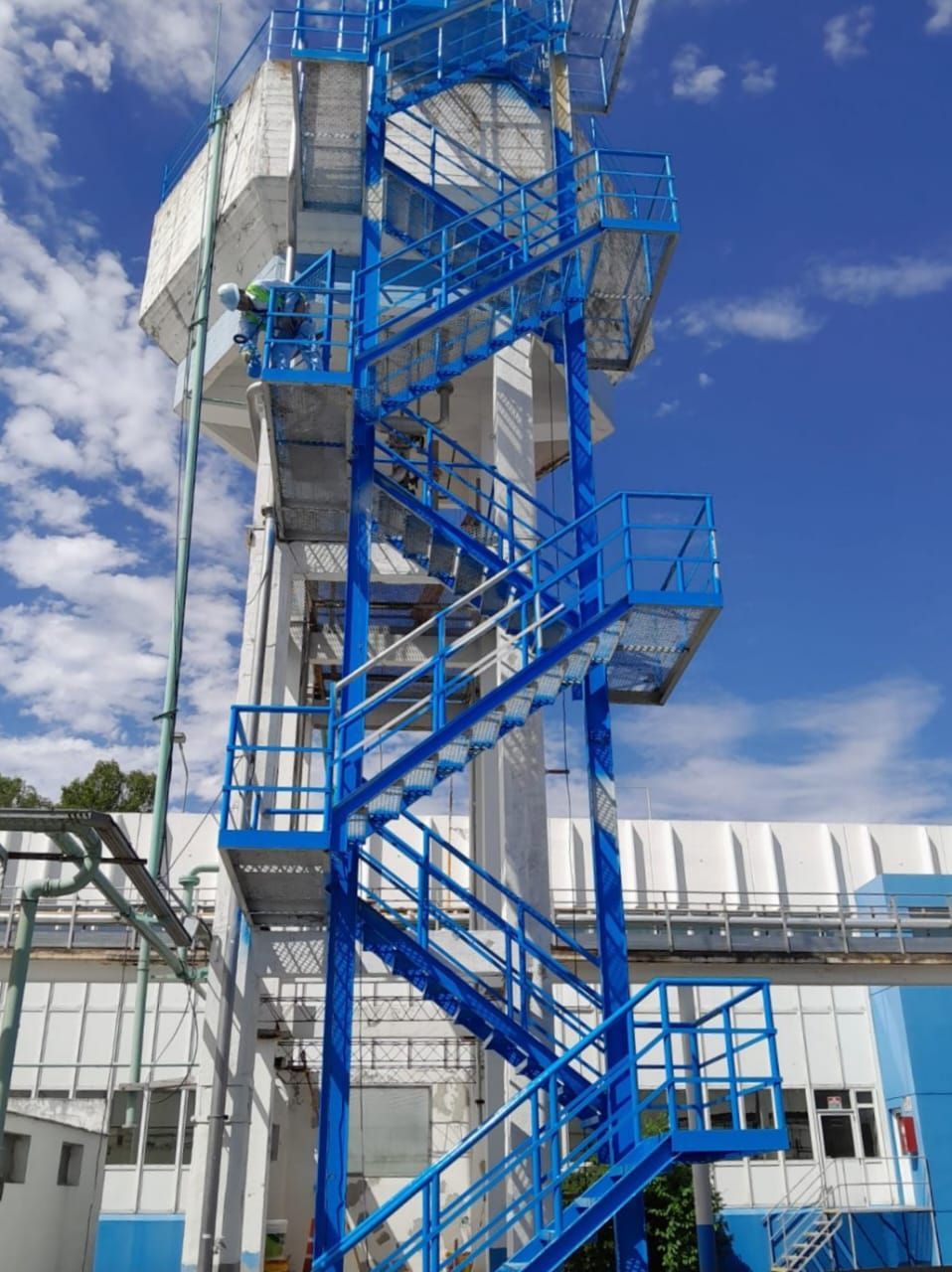 Escalera exterior de metal azul en un edificio alto blanco contra un cielo azul.
