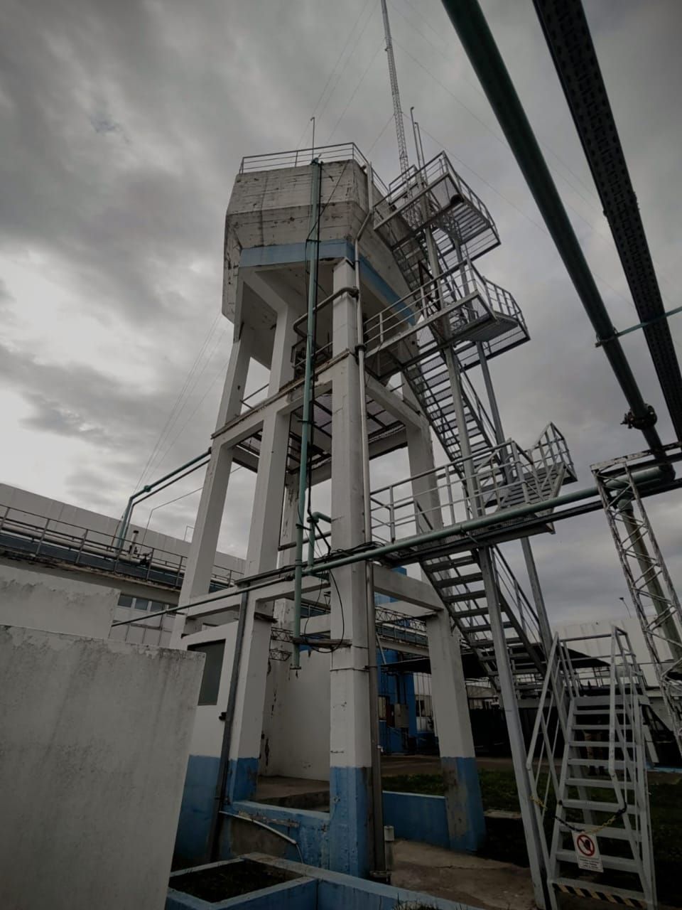 Una torre de agua de hormigón con escaleras de metal contra un cielo nublado.