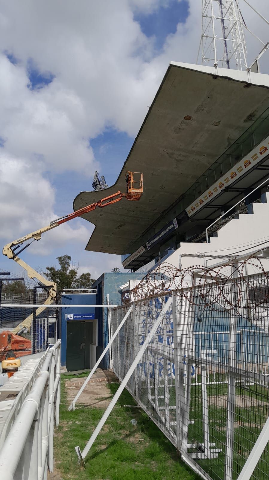 Persona en un ascensor trabajando en el techo del estadio bajo un cielo nublado.