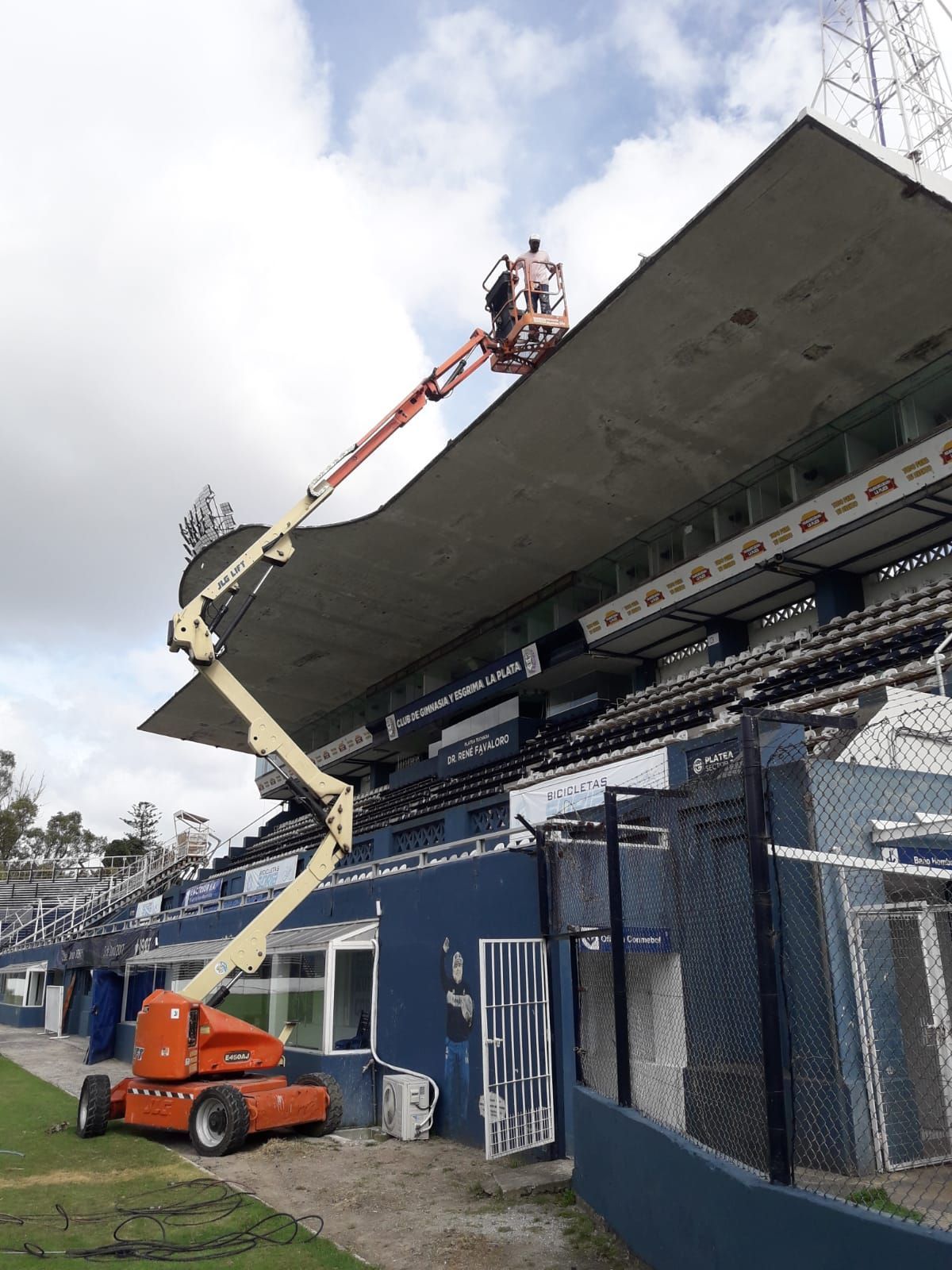 Trabajadores en una plataforma elevadora reparando el techo de un estadio. 