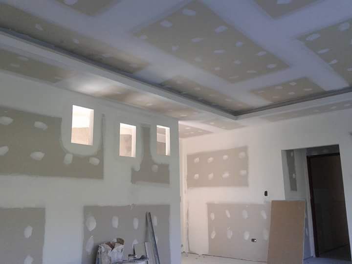 Habitación interior en construcción; drywall instalado en paredes, techo con paneles empotrados y tres marcos de ventanas.