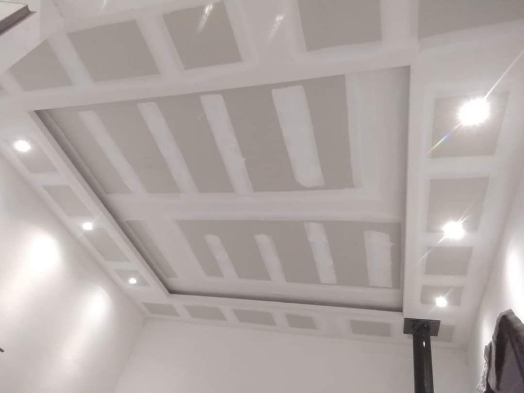 Techo de yeso terminado con luces empotradas. Paredes blancas, yeso gris claro y viga de soporte negra.