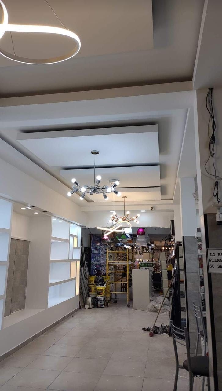 Vista interior de una tienda con estantes blancos, artefactos de iluminación y varios artículos en la parte trasera.