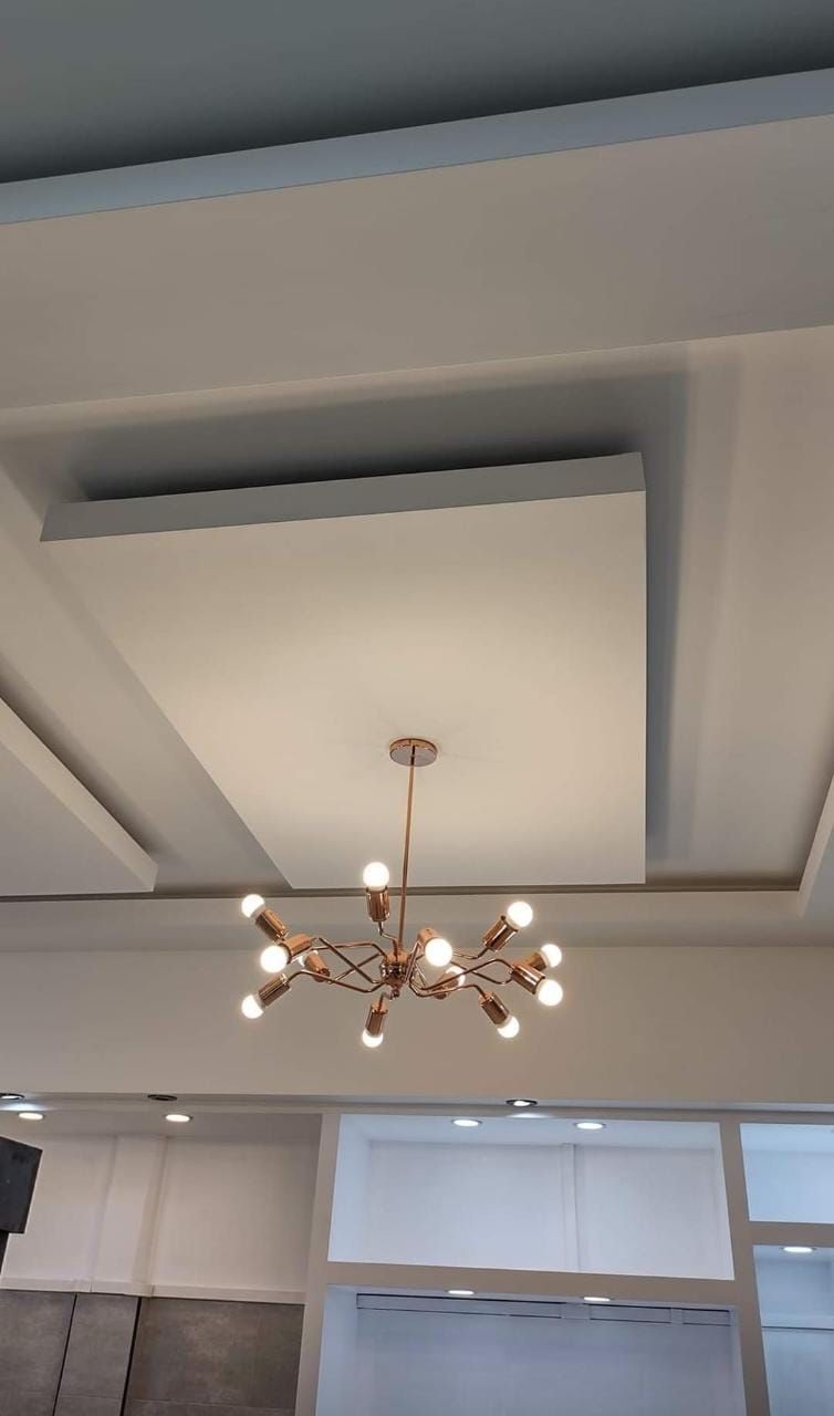 Lámpara de araña moderna colgada de un techo blanco con cuadrados empotrados, en una habitación luminosa.