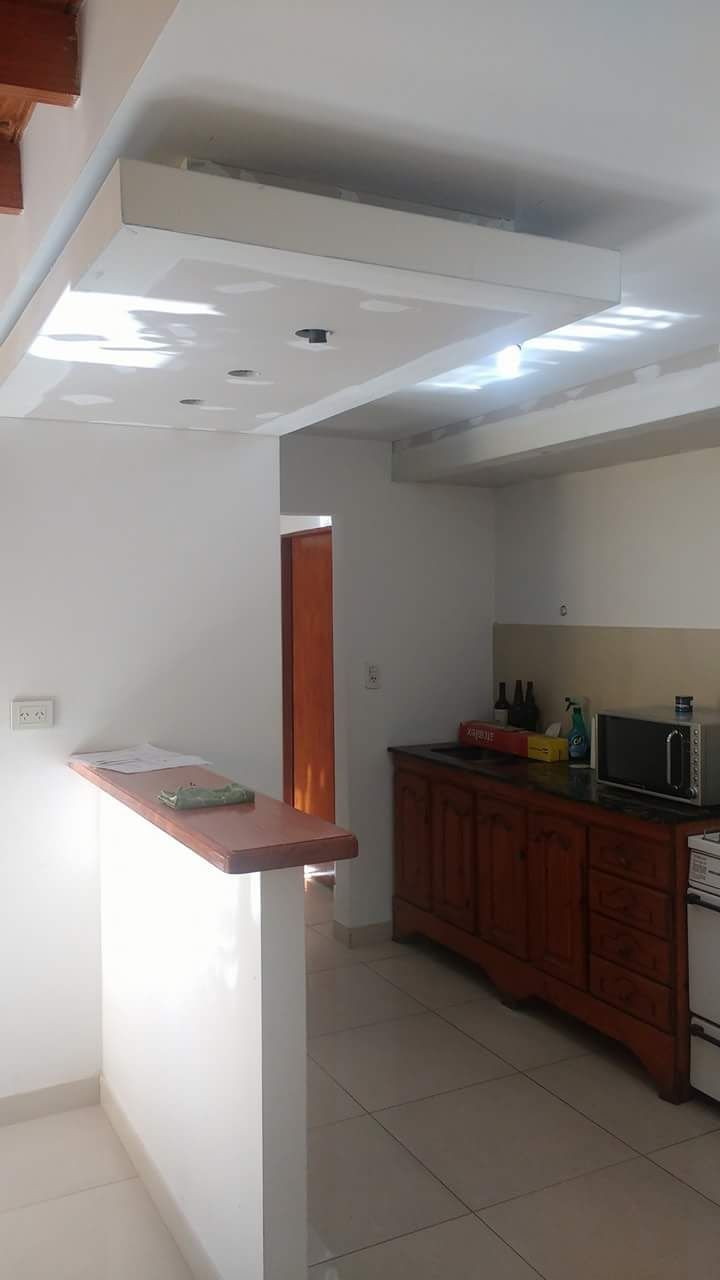 Interior de cocina con pared blanca y armarios de madera. La puerta da a otra habitación.