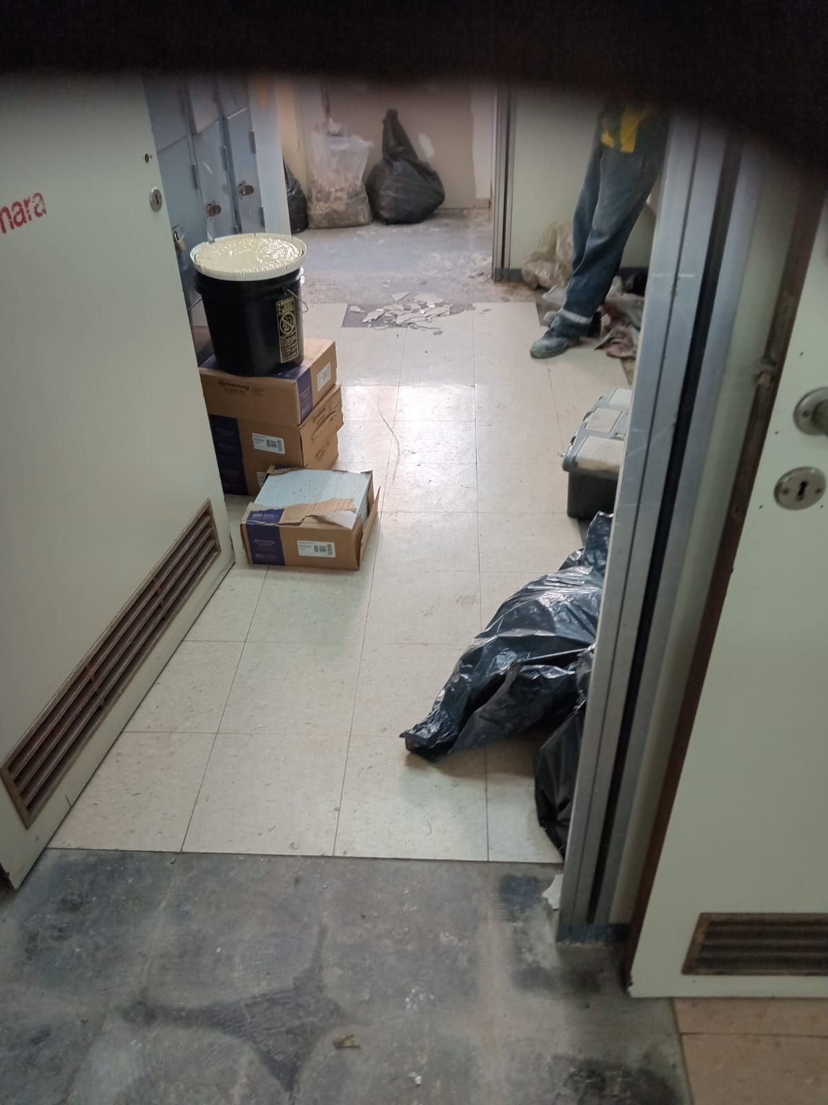 Habitación estrecha con cajas, bolsas de basura, un cubo de pintura y una persona de pie. Puertas a ambos lados.