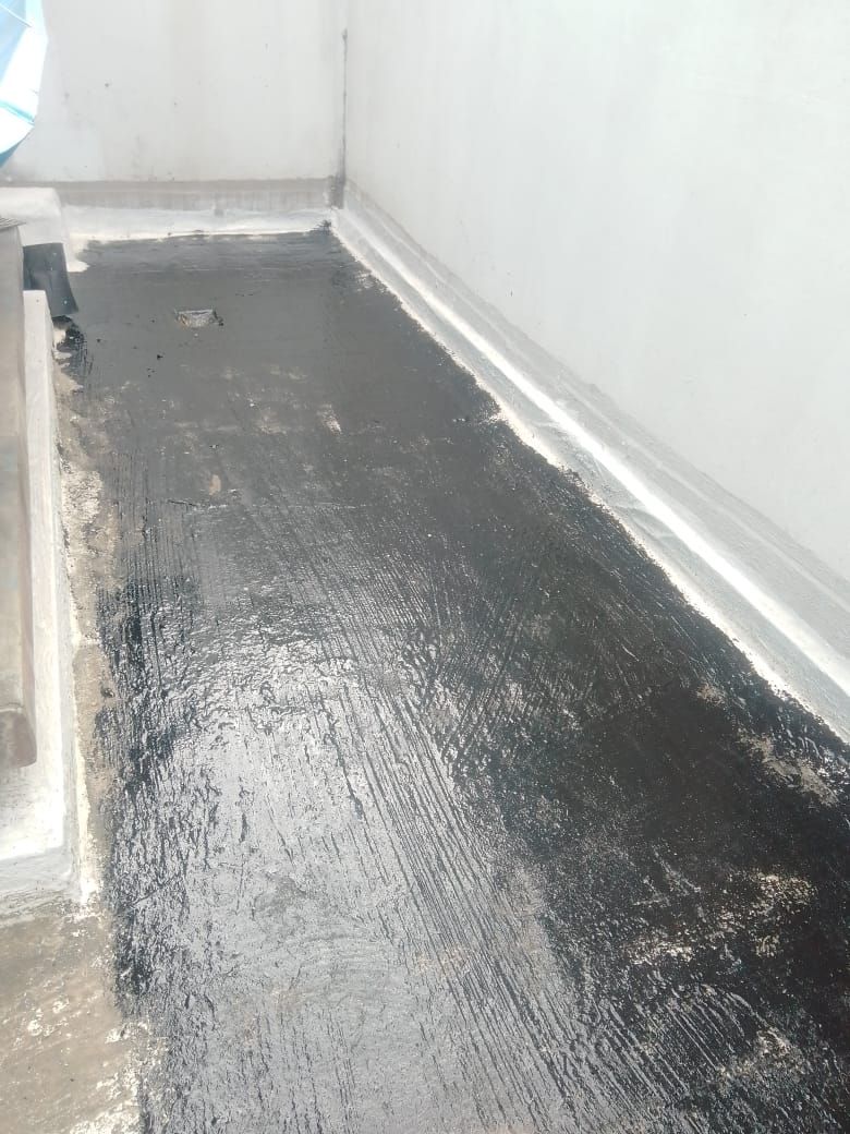 Revestimiento impermeable negro aplicado sobre un suelo al lado de una pared blanca.