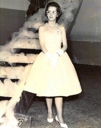 Woman in a formal dress, gloves, and heels stands on a staircase decorated with 