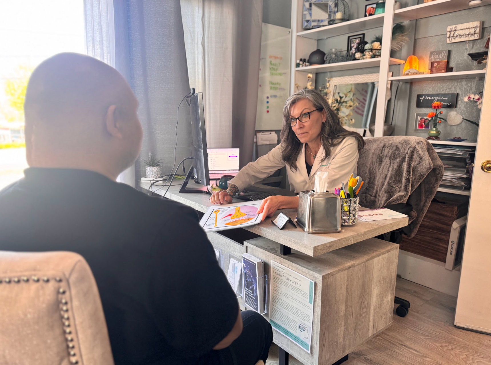 A professional sitting at a desk consults with a patient, holding a colorful informational brochure.