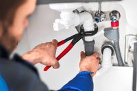 Plumber using red-handled pliers to fix under-sink pipes and fittings