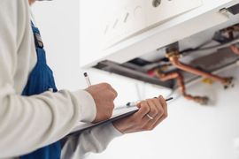 Technician inspecting the underside of a wall-mounted boiler with a clipboard