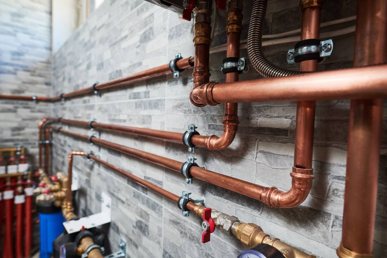 Copper pipes and valves installed along a gray brick wall in a basement utility room