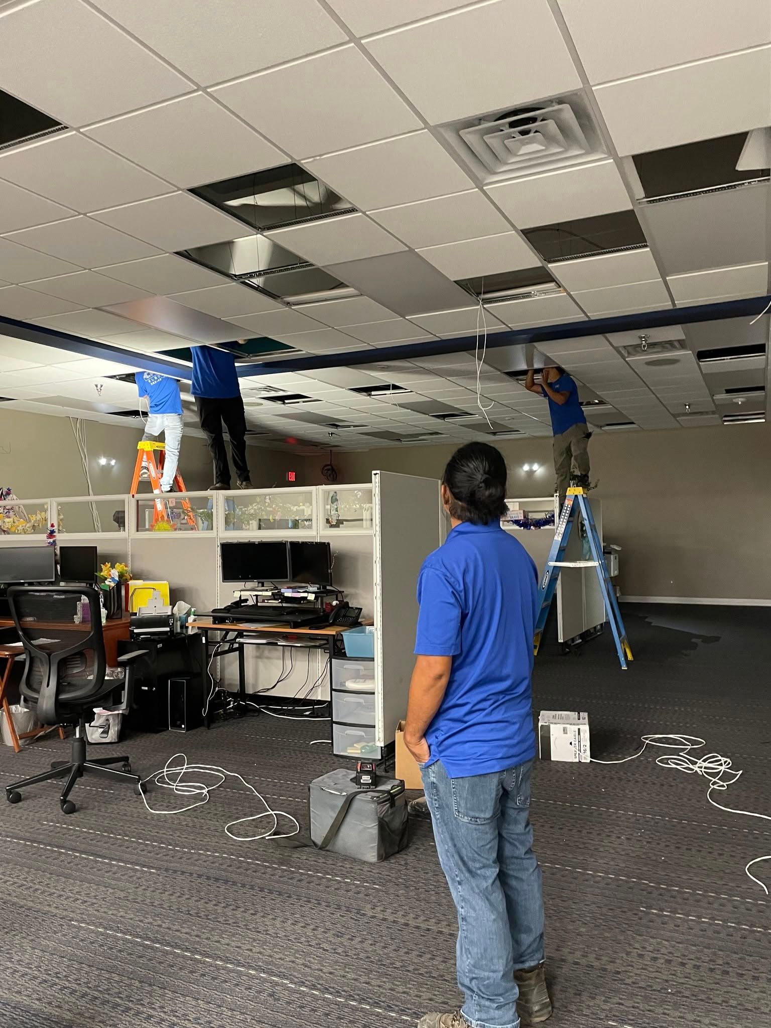 A group of men are working on the ceiling of an office building.