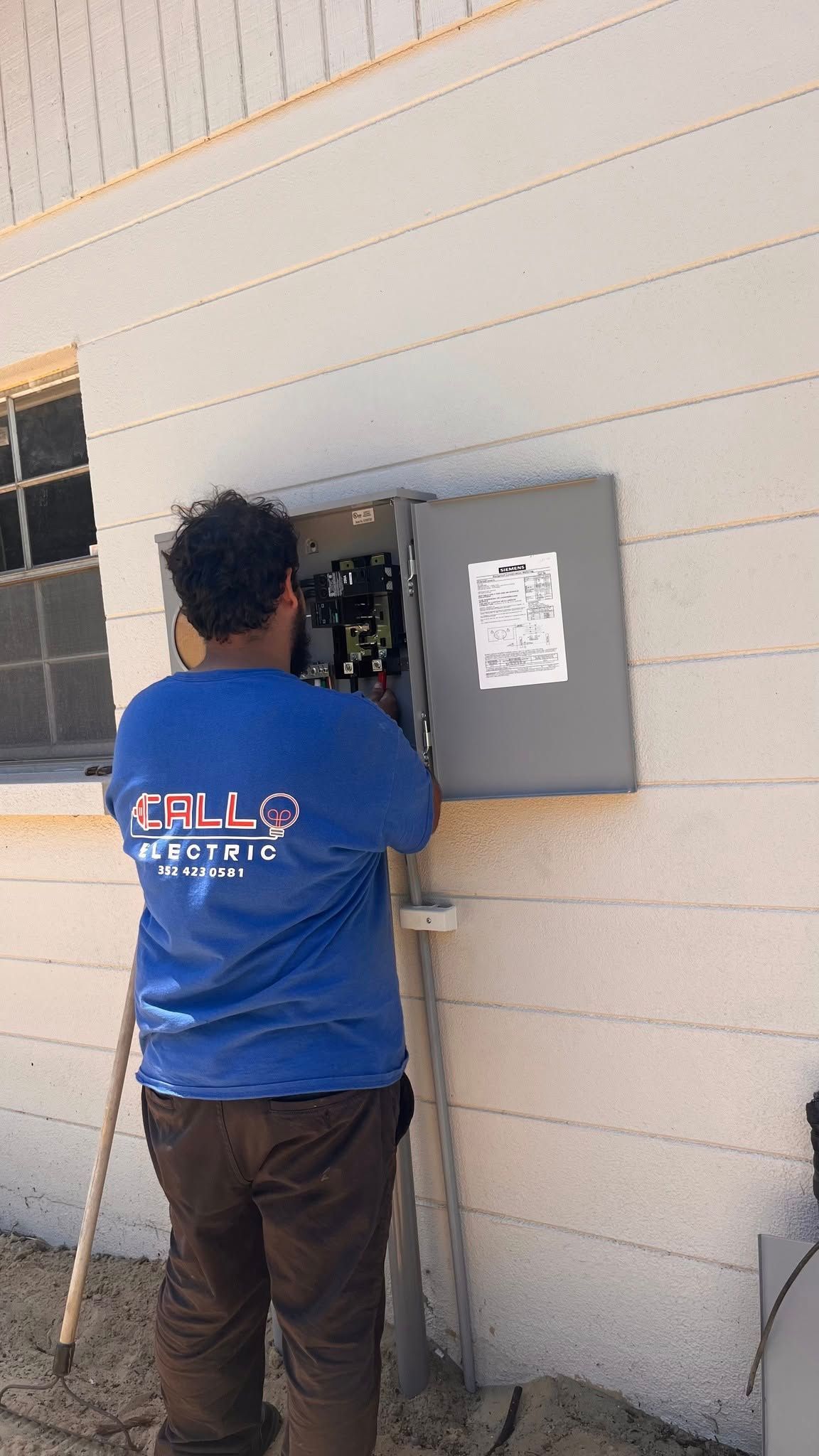 A man in a blue shirt is working on an electrical box on the side of a building.
