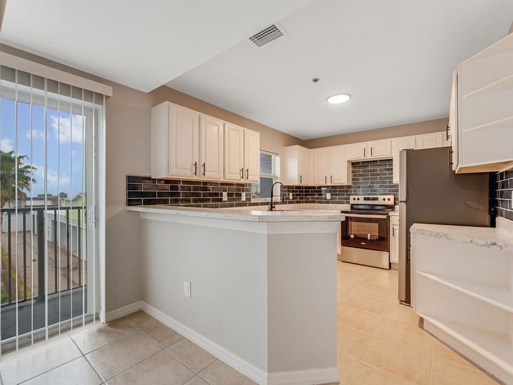 Kitchen with light cabinets, stainless steel appliances, and a sliding glass door to a balcony.