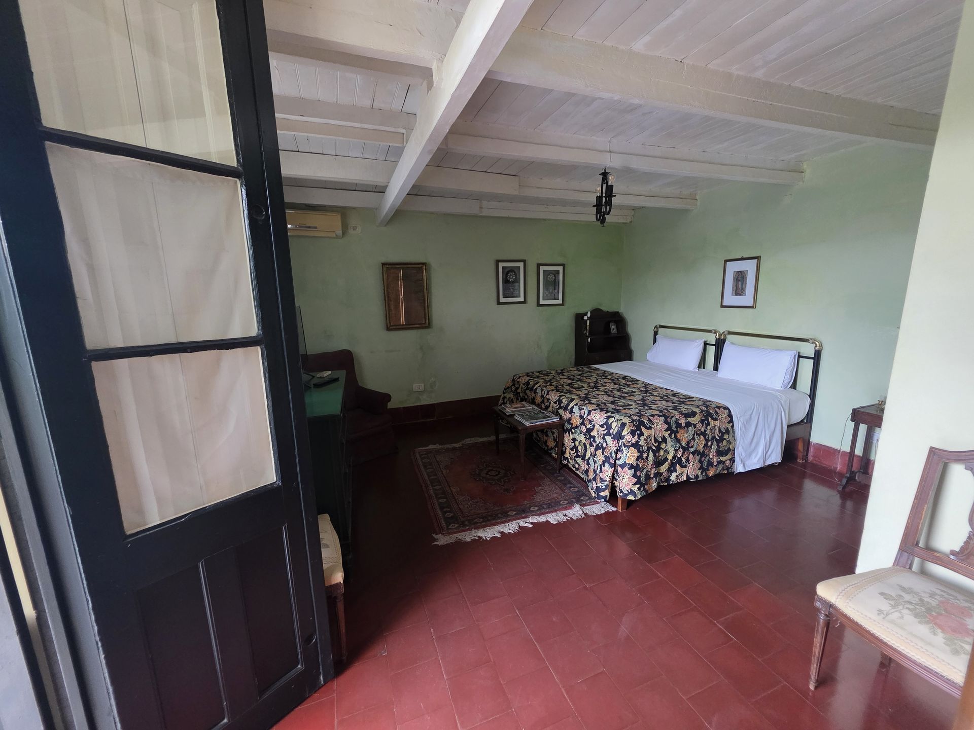 Dormitorio con cama doble, muebles antiguos, suelos de madera y paredes verdes. La puerta abierta ofrece vistas al exterior.