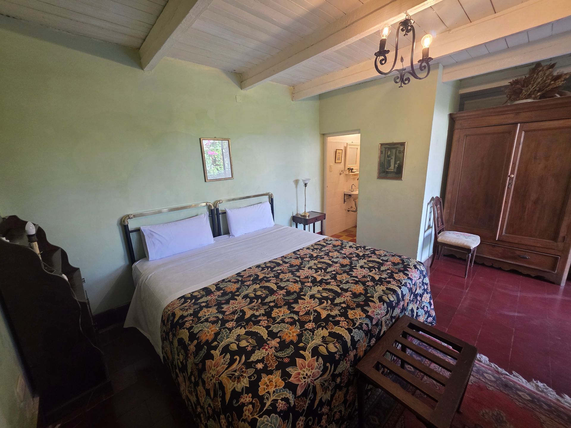 Dormitorio con cama de matrimonio, edredón con estampado floral y armario de madera sobre suelo rojo.