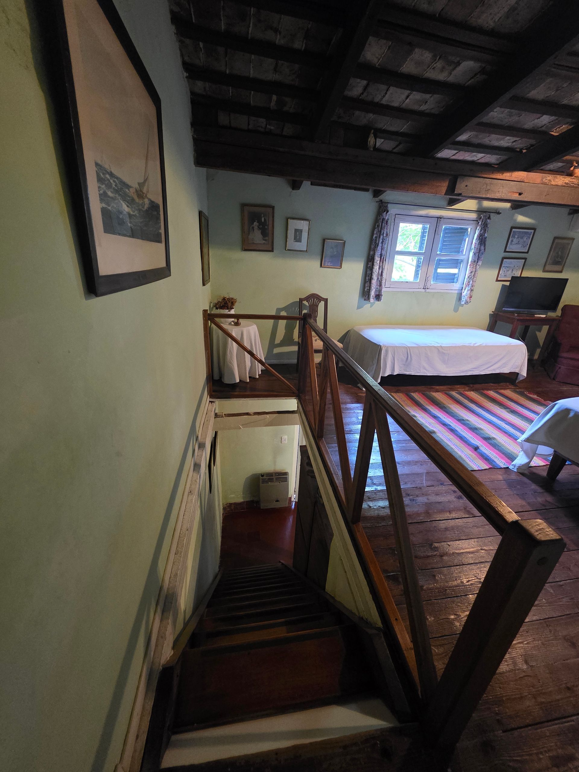 Vista interior de una habitación rústica con escalera y zona de loft con cama y mesa.