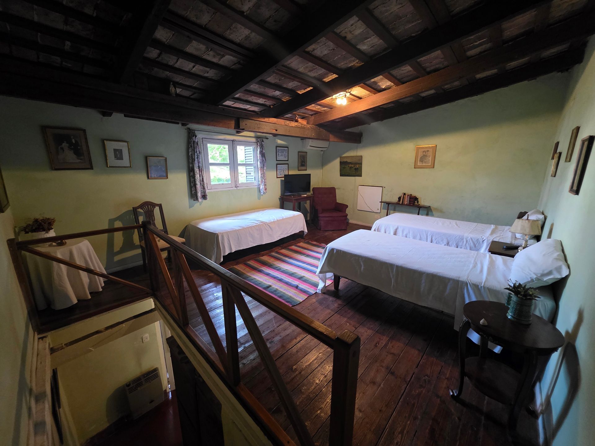 Dormitorio con tres camas, suelo de madera, vigas del techo a la vista y una pequeña mesa redonda.