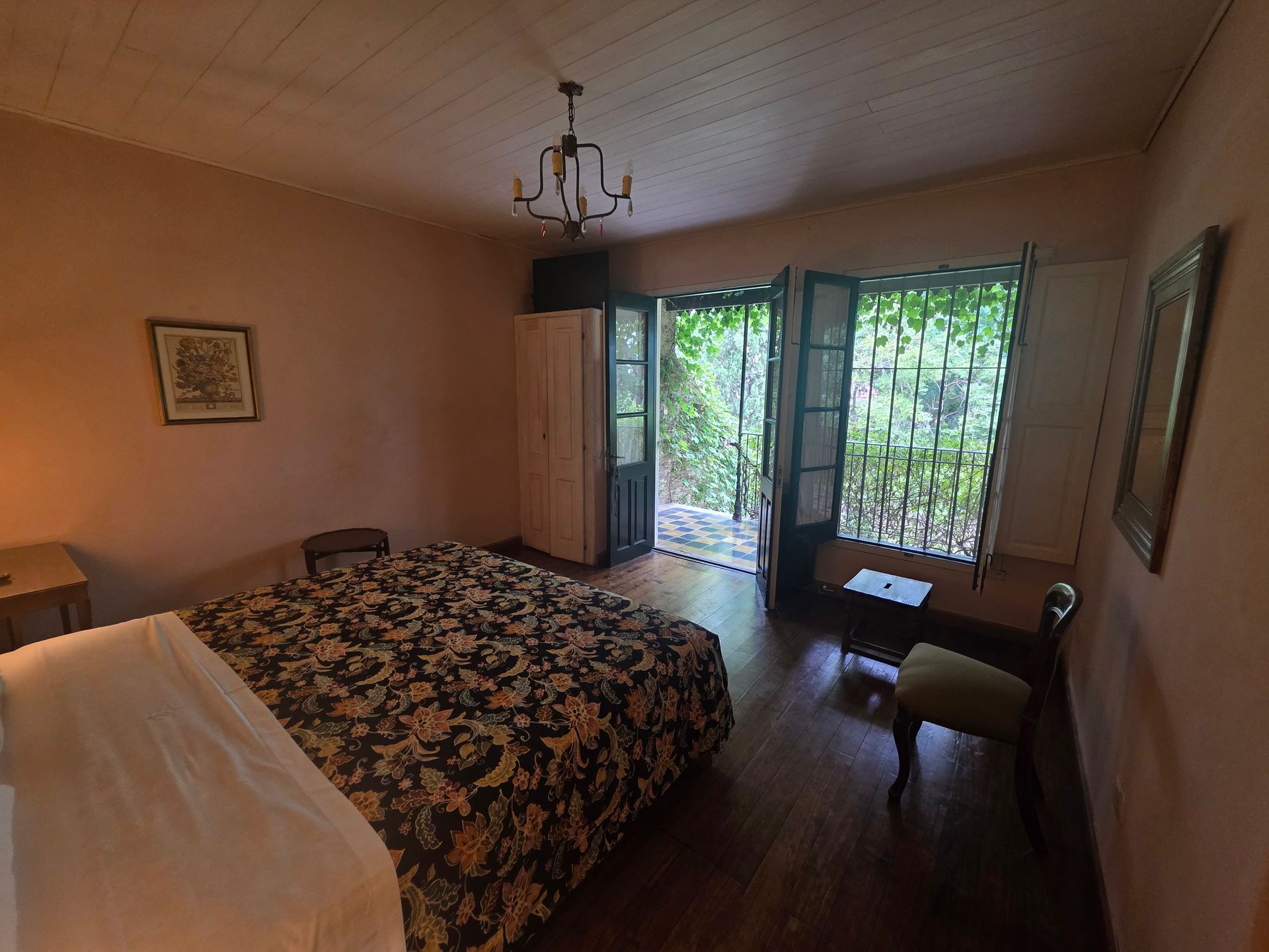 Dormitorio con cama, puertas abiertas a zona verde y suelos de madera.