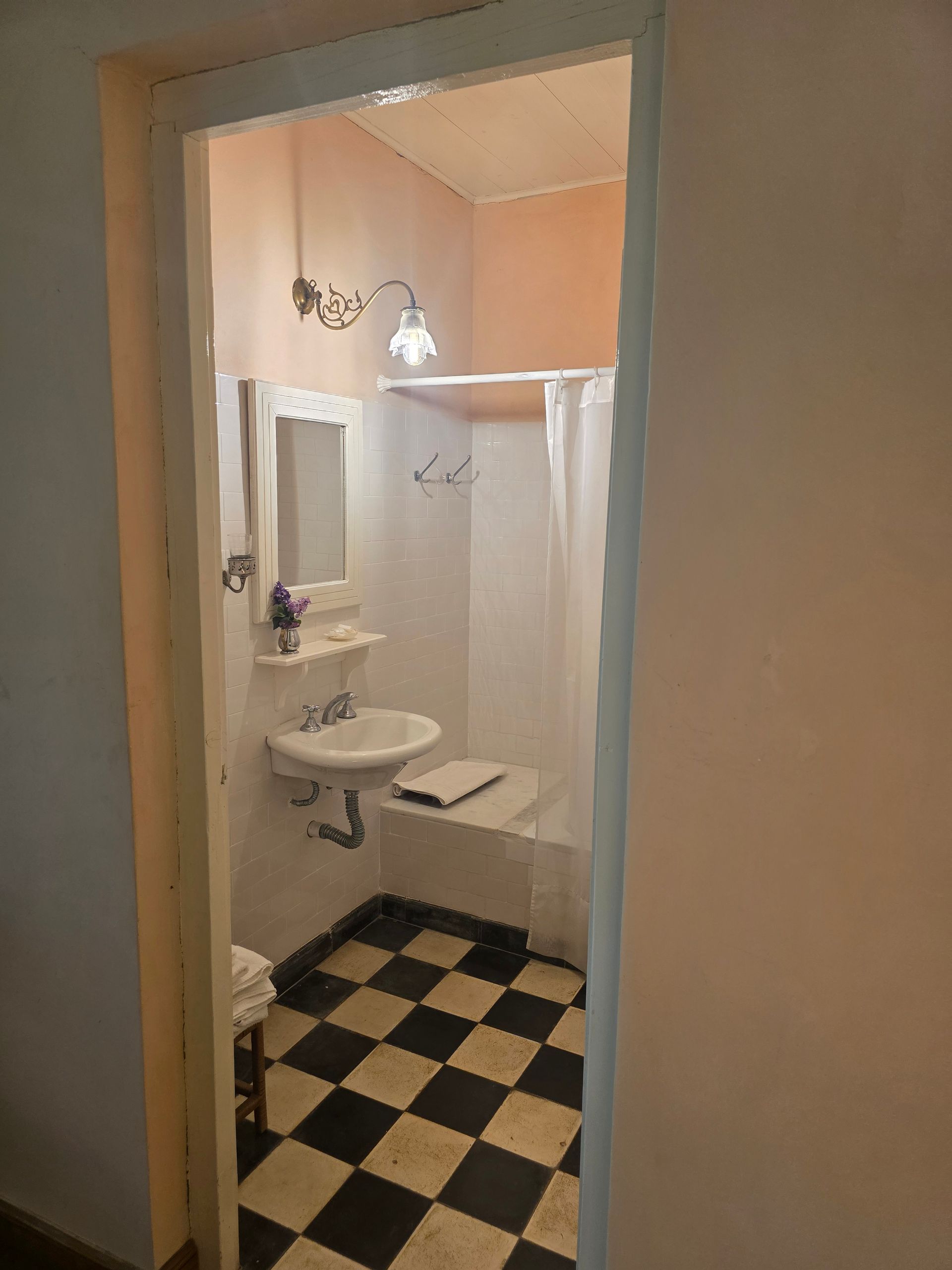 Baño con suelo a cuadros en blanco y negro, lavabo, espejo y ducha.