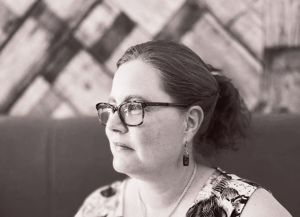 Woman with glasses, ponytail, and floral top in a restaurant, looking off to the side.
